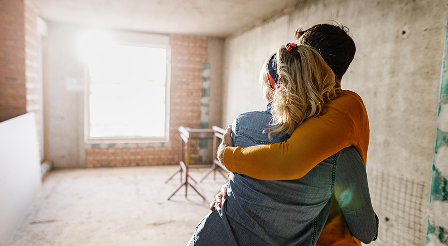 Man and woman hug as they stare at empty room under construction